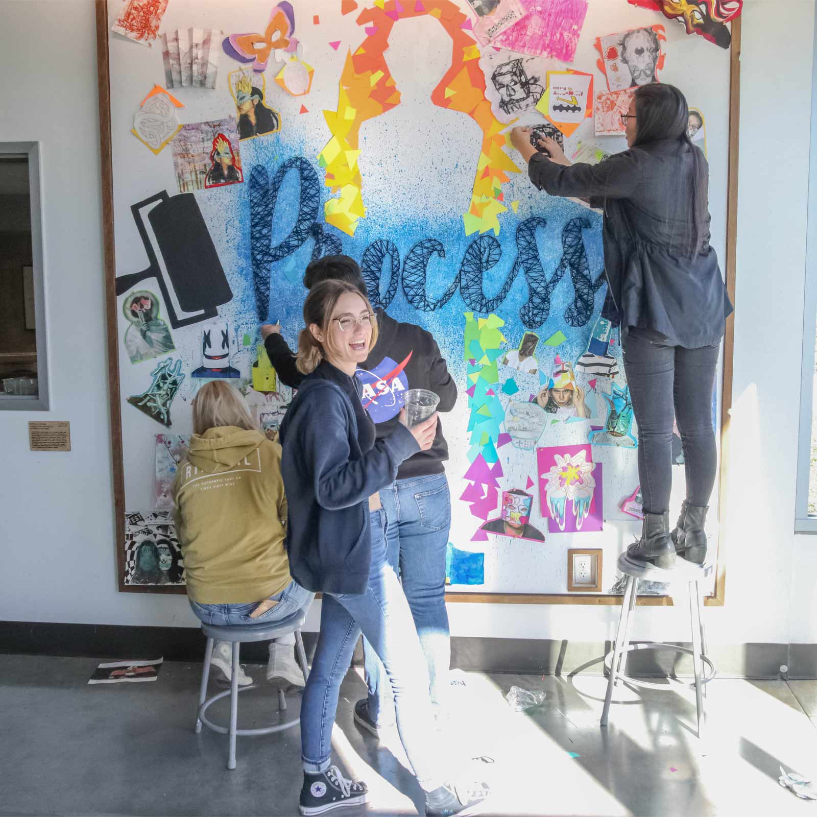 Students working on a collage mural with the word "Process" at the center